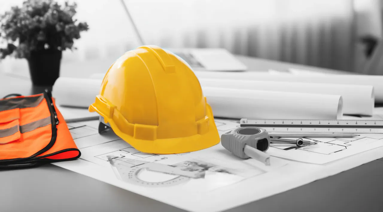 A hard hat and drawings on a desk, where the relationship is managed from