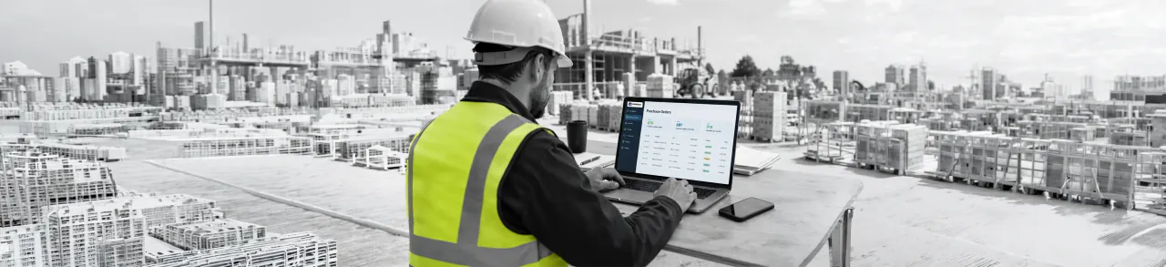 Construction worker reviewing purchase orders on a laptop at a building site