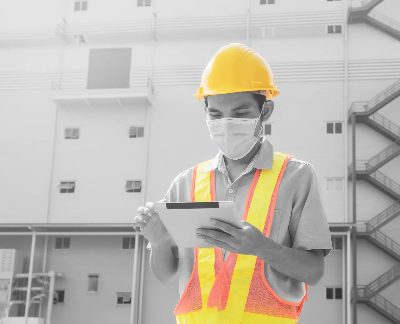 Construction worker in a yellow hard hat and high-visibility vest using a tablet