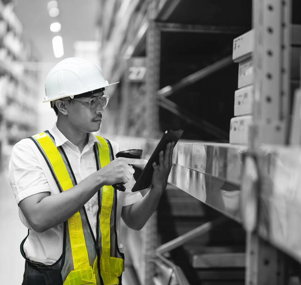 Site worker in hi-vis and a hard hat scanning a labelled stock location with a handheld scanner and a tablet in a warehouse aisle