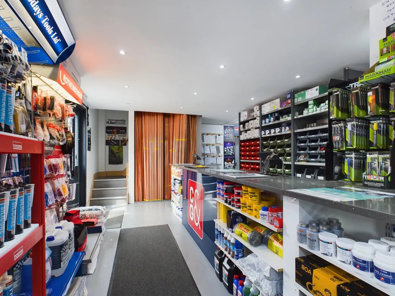 The C&amp;G trade counter seen from the far end, with copper tube racked behind it and flux, steel wool, pipe cement and jointing compound shelved along the counter