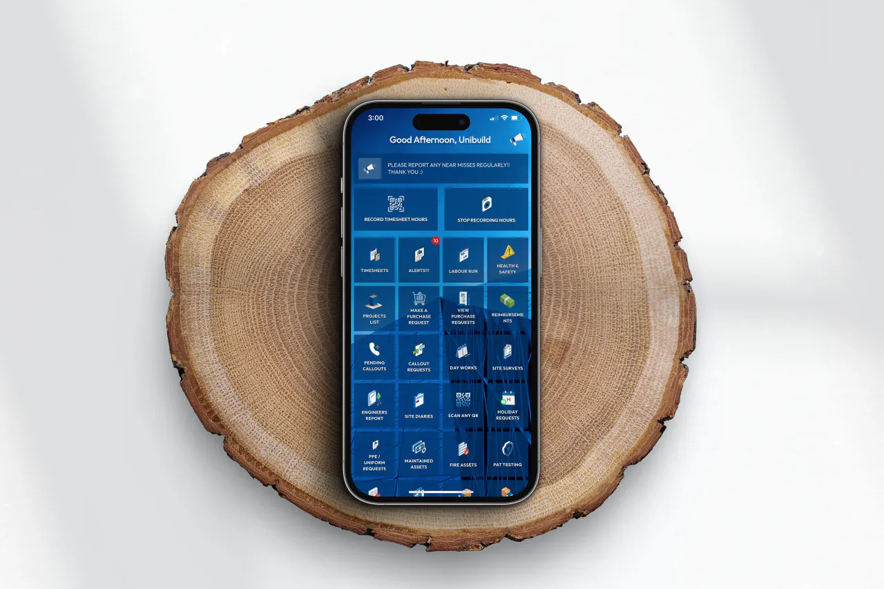 A phone on a wood slice, open on the SME Building Services app home screen