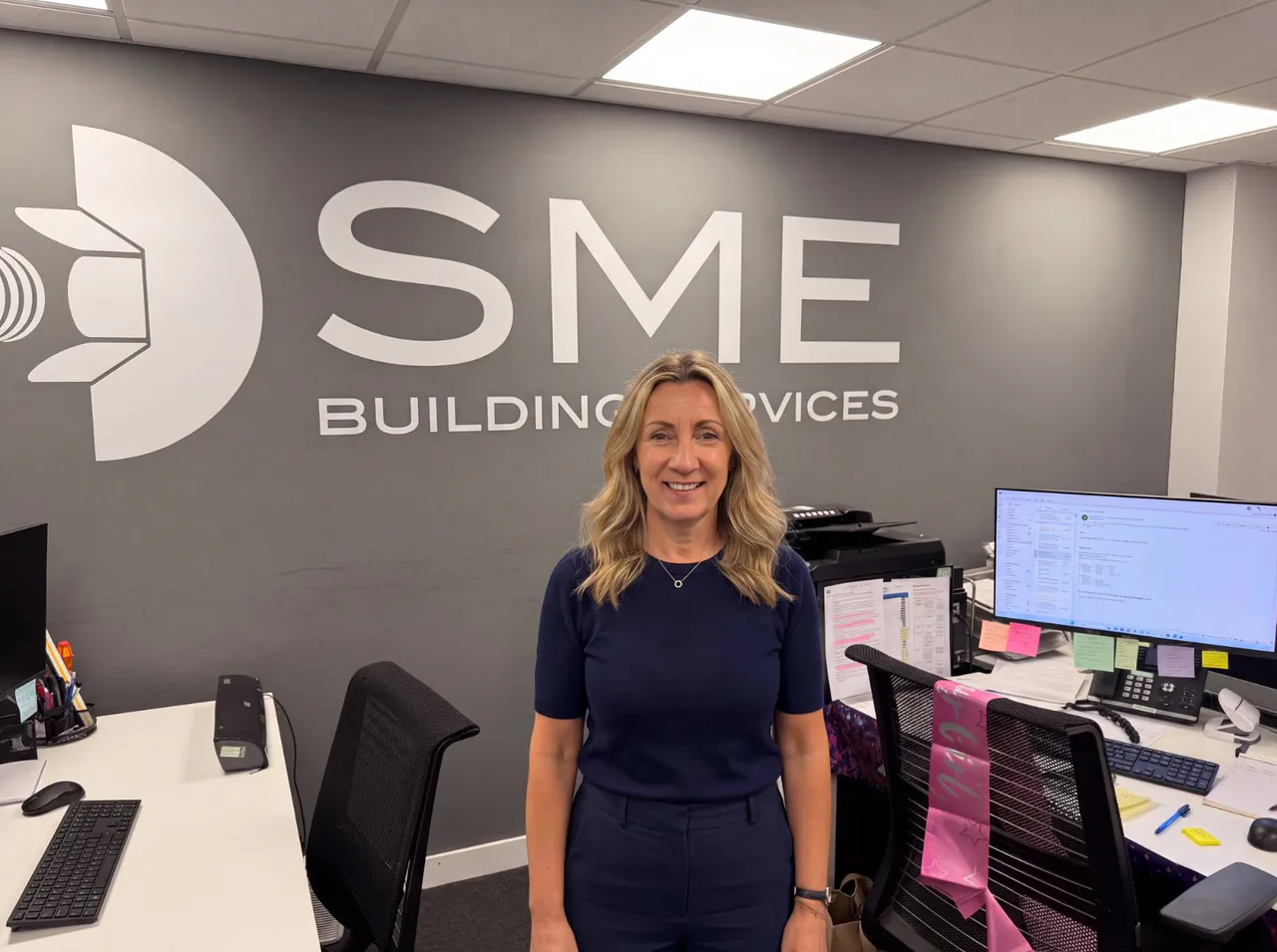 Niki Scarth, office administrator at SME Building Services, standing in the firm’s Croydon office with the SME Building Services mark on the wall behind her