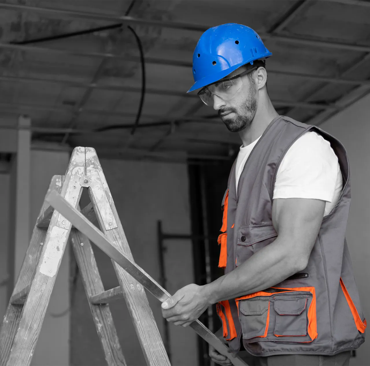 Tradesperson in a hard hat and safety glasses holding a level beside a stepladder