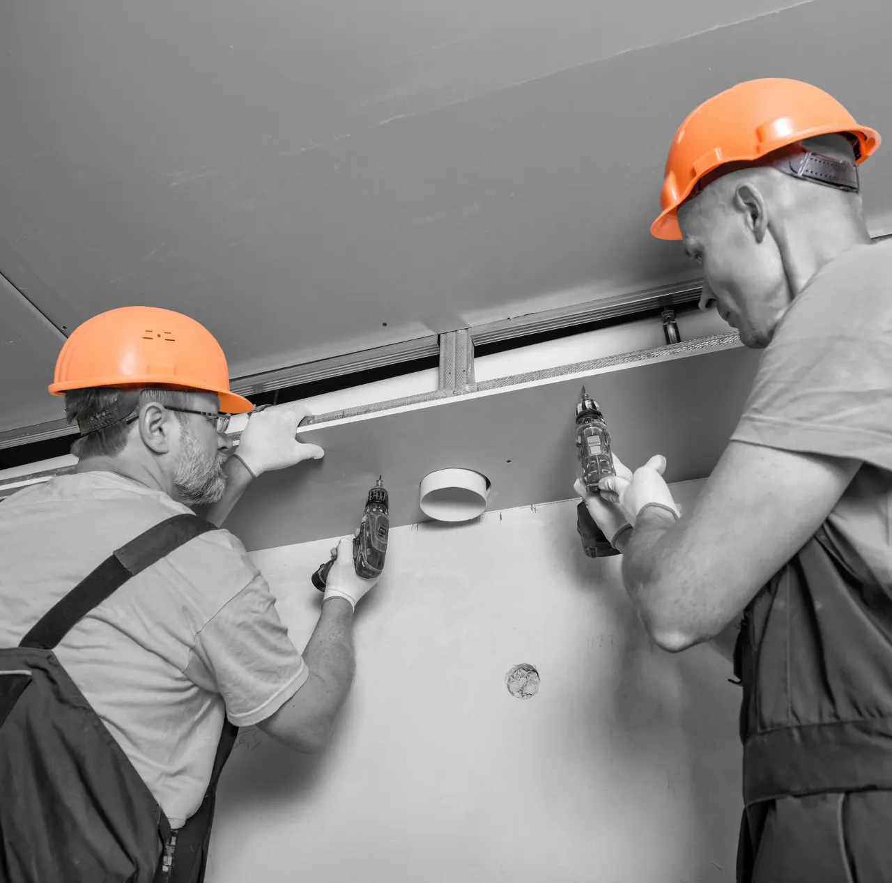 Two operatives in hard hats drilling fixings into a ceiling panel