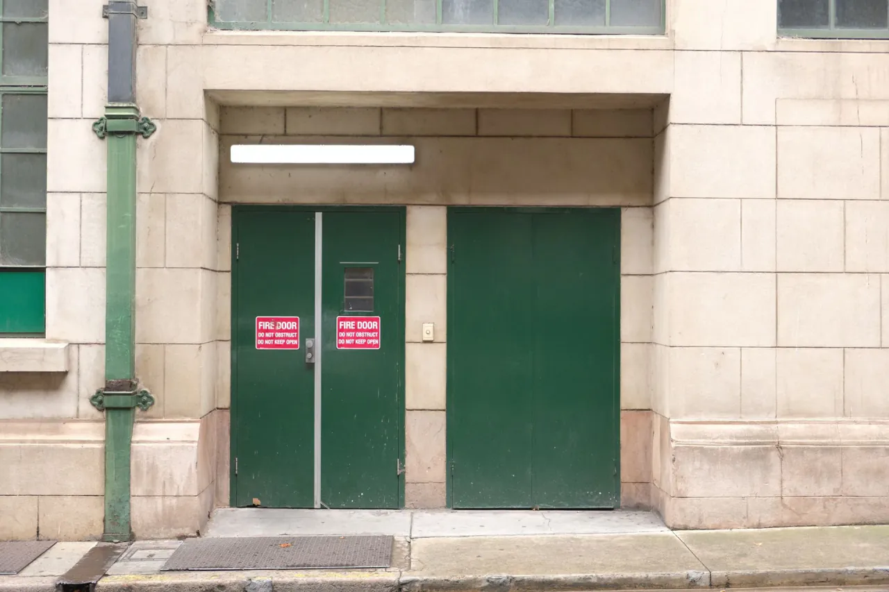 A pair of green fire doors carrying fire door signage on a city street