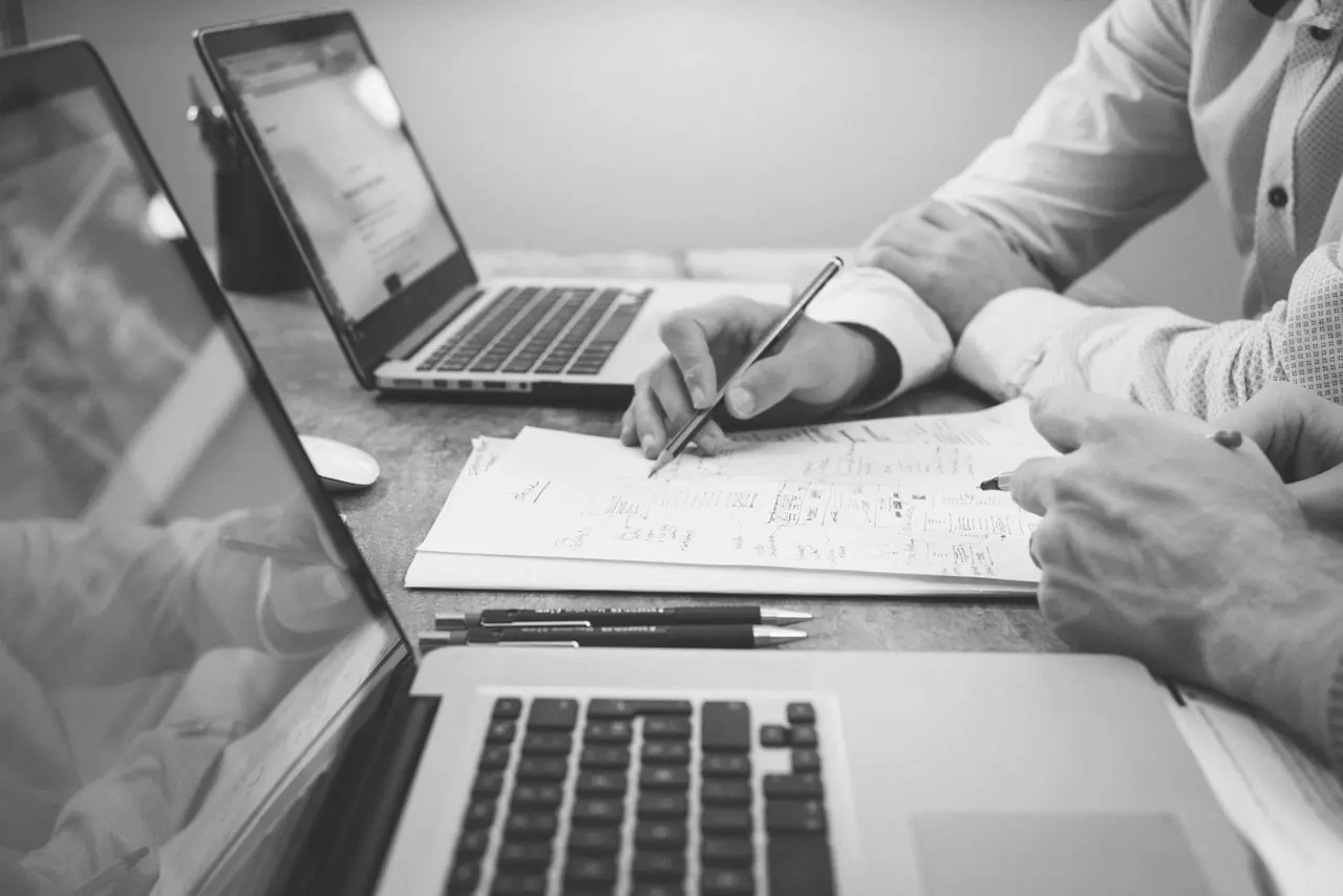 Two people working through a drawing at a desk with laptops