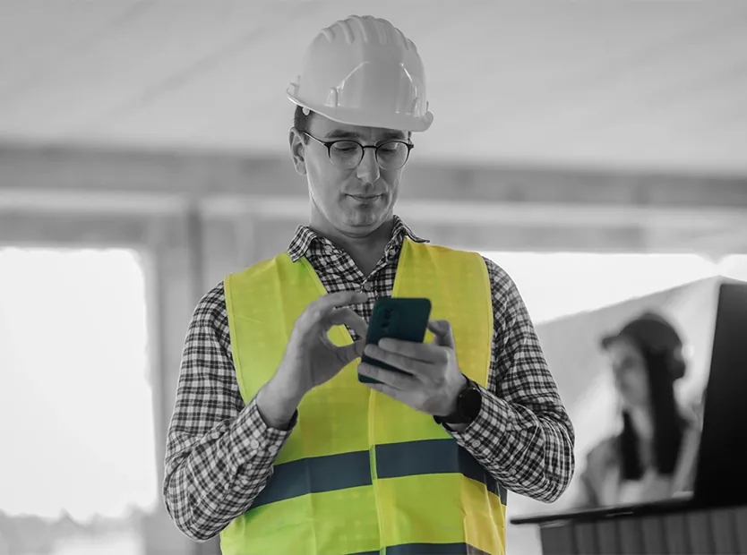 Site supervisor in hi-vis checking a phone on a UK construction site
