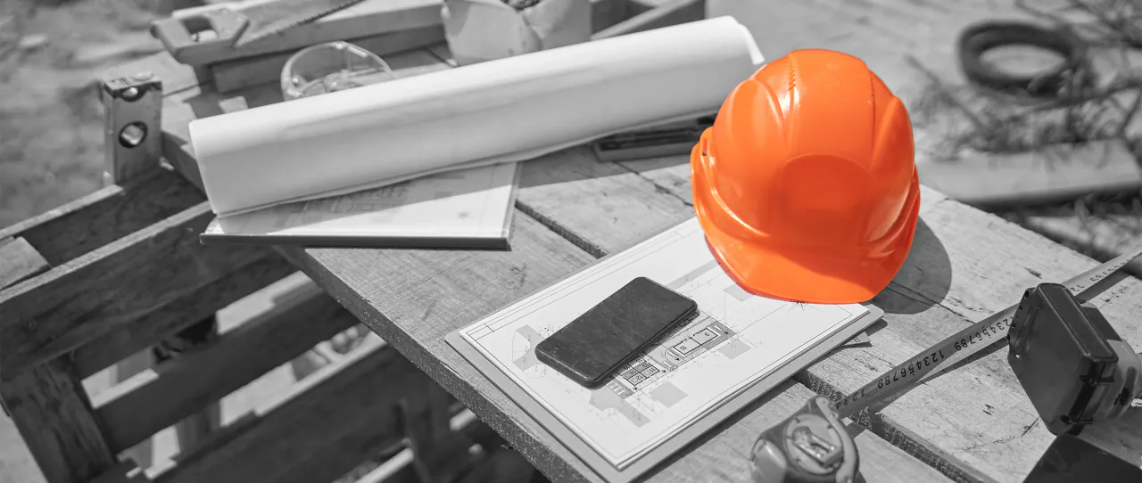 Hard hat, rolled drawings and a phone on a site bench